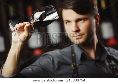 Bokal of red wine on background of male sommelier appreciating color, quality, flavor and sediments of drink. Professional degustation expert in winemaking.