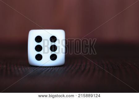 Single white plastic dice on brown wooden board background. Six side cube with black dots. Number 6.