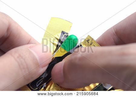 Hands tearing blister pack of green and yellow capsule medical pill.