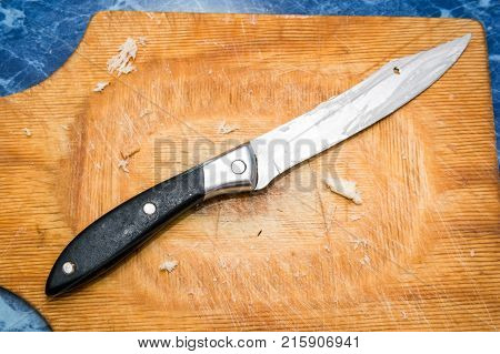 Close up kitchen knife with black handle on wooden cutting board covered with bread crumbles