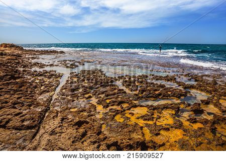 Fisherman with a long rod on coastal stones. North of Israel, on the Mediterranean coast. The concept of sports tourism