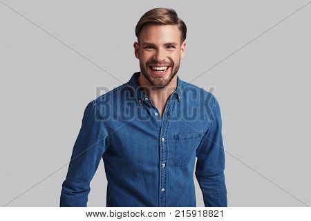 Simply charming. Handsome young man smiling and looking at camera while standing against grey background