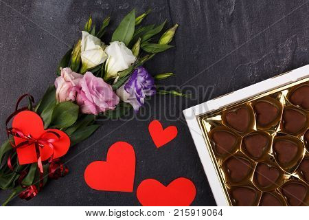 A bouquet of Japanese roses and a box of chocolates showing not completely with carved hearts on a stone background