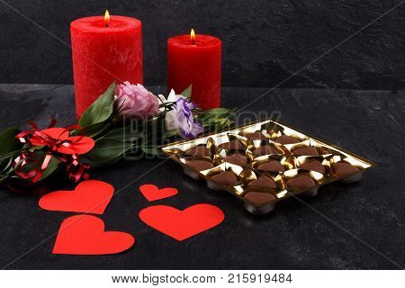A bouquet of Japanese roses tied with a ribbon with burning candles and a box of chocolates on a stone background