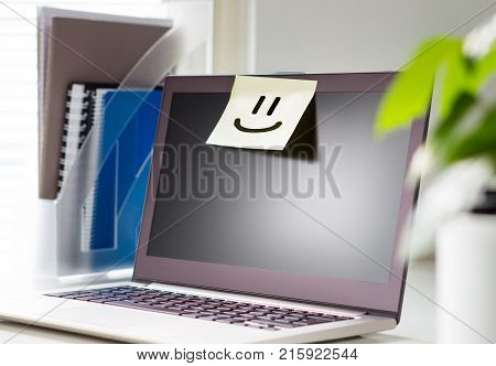 Good working environment and happy atmosphere in workplace. Team spirit. Smiley face drawn on a sticky paper and post it note on laptop in office workstation.