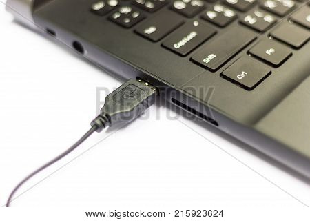 Closeup - USB cable connect to USB slot on laptop on white table