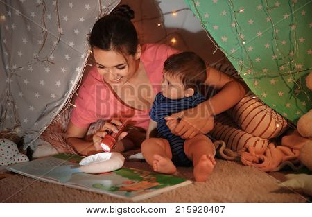 Young mother with little son reading book in hovel at home