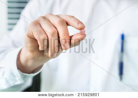 Doctor or pharmacist holding one pill between fingers. Medical professional and expert in white coat with medicine.
