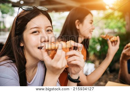 Asian students eating eating the pizza together in breaking time early next study class having fun and enjoy party Italian food slice with cheese delicious at university outdoor.