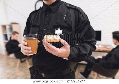 Police officers eat donuts and drink coffee at the police station. They rest in the break of work. They are in a good mood, they are smiling.
