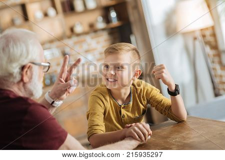 Armwrestling game. Positive happy nice grandfather and grandson looking at each other and having fun while doing armwrestling