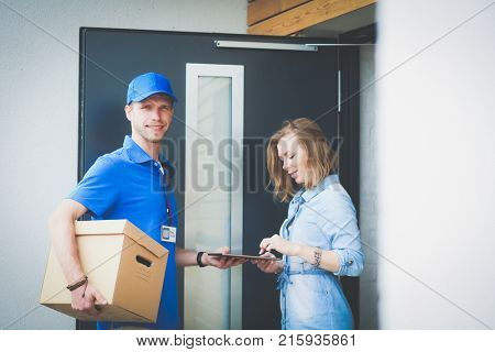 Smiling delivery man in blue uniform delivering parcel box to recipient - courier service concept. Smiling delivery man in blue uniform