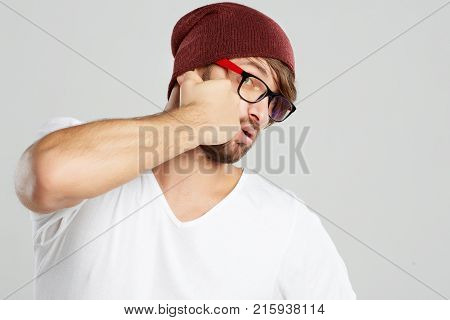 Shot of a bearded young man wearing glasses and a hat punching himself in the face on grey background copyspace self destruction depression self esteem mistake punishman fighting punch.