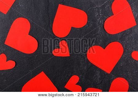 Red hearts of different sizes are scattered close-up on a stone background. View from above