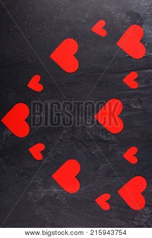 The hearts are red, carved in different sizes lined up in one big heart lying vertically on a stone background