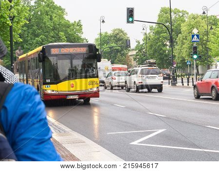 WARSAW POLAND - MAY 24 2017: Bus approaching stop in Warsaw while people are waiting in the platform. Varsovian buses can be recognized by their yellow and red color.