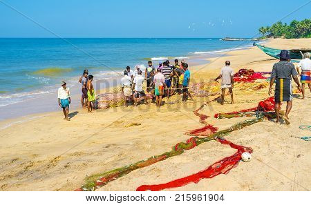 BENTOTA SRI LANKA - DECEMBER 6 2016: The fishermen manually pull their net out of the ocean and consider their successful catch on December 6 in Bentota.