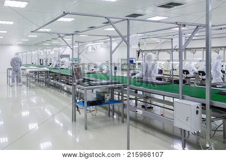factory workers in white lab suits and face masks, producing tv sets on assebly line with some modern equipment