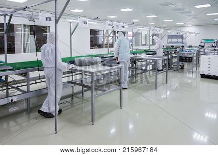factory workers in white lab suits and face masks, producing tv sets on assebly line with some modern equipment