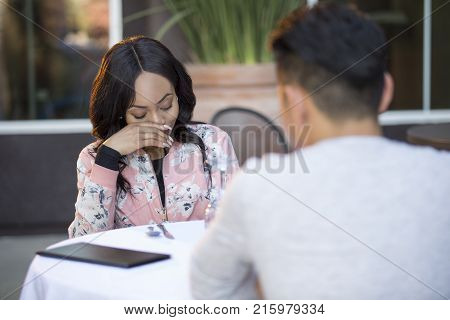 Black female disinterested with a blind date at an outdoor restaurant. They are sitting and chatting like speed dating. The image depicts relationship problems.