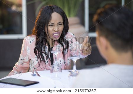 Black female disinterested with a blind date at an outdoor restaurant. They are sitting and chatting like speed dating. The image depicts relationship problems.