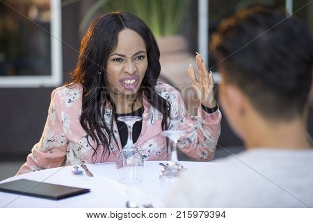 Black female disinterested with a blind date at an outdoor restaurant. They are sitting and chatting like speed dating. The image depicts relationship problems.
