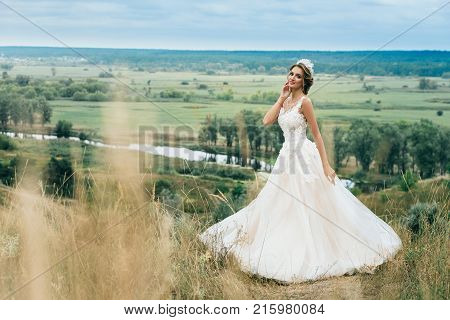 Portrait Of A Young Beautiful Bride On A Background Of A Gorgeous View Of The River And Fields.