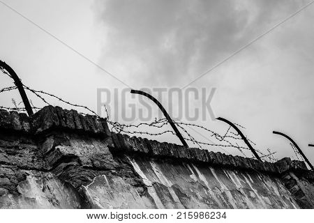 Ominous barbwired concrete wall of the concentration camp Terezin with storm clouds in the background - Black and White