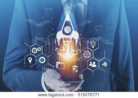 Businessman Looking At Smartphone With Double Exposure Of Startup Rocket Hologram. Concept Of Busine