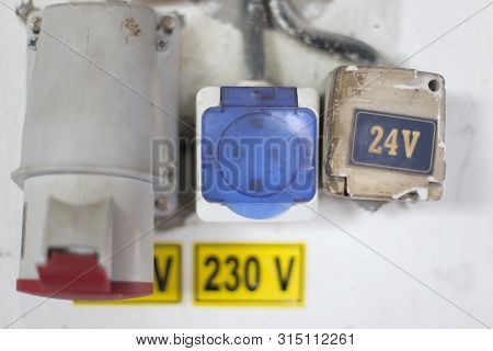 Worn Out 400v, 230v And 24 Industrial And Multiphase Power Plugs And Sockets On A Dirty Wall Inside 