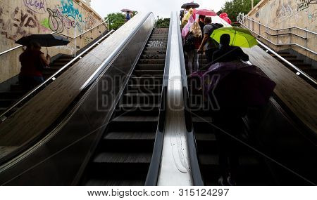Bucharest, Romania - July 29, 2019: People With Rain Umbrellas Opened Go Up And Down The Escalators 