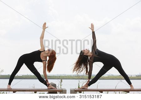 Two Young Women Doing Yoga At Nature. Fitness, Sport, Yoga And Healthy Lifestyle Concept - Group Of