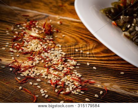 Rosemary And Sesame Spices Near White Plate On Wooden Background.