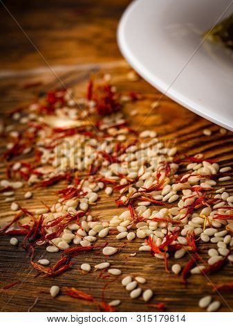 Rosemary And Sesame Spices Near White Plate On Wooden Background.