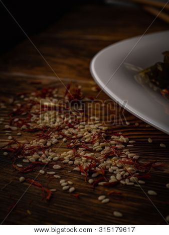 Rosemary And Sesame Spices Near White Plate On Wooden Background.