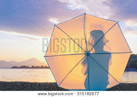 Silhouette Of Young Boy Hipster In Hat With Umbrella. Kid With Umbrella Looking At Seascape. Travell