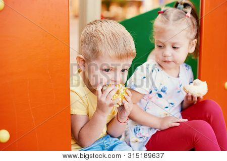 Cute Toddler Boy And Girl Is Eating Donuts Outdoor. Children Is Having Fun With Cakes. Tasty Food Fo