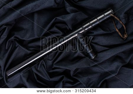 Black Rubber Police Baton On Black Shirt Wrinkled Cloth Low-key Flat Lay