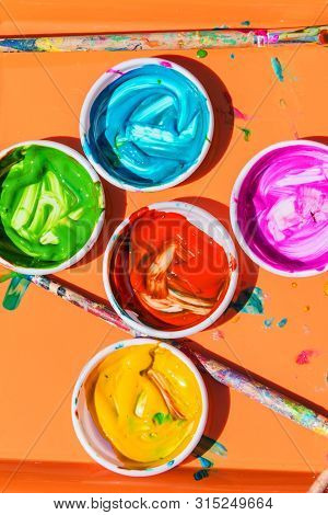 Ceramic Bowls Filled With Colorful Paints And Paint Brushes Sit On Paper For Kids To Use To Paint Wi