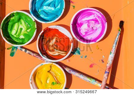 Colorful Paints Sit In Containers With Paint Brushes Laying Nearby, For Kids To Create Art Projects 