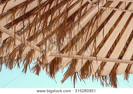 Part Of A Wooden Beach Umbrella With Palm Branches On The Background Of The Azure Sky
