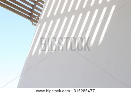 Shadow From The Striped Lattice On A White Wall Against The Blue Sky In Sunny Weather