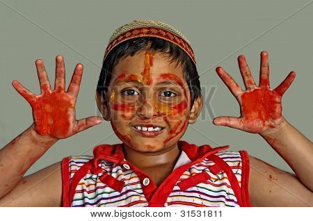 Giovane felice Asian Bengali ragazzo giocando Holi, sorridente con colori su viso e mani, cappuccio sulla testa,