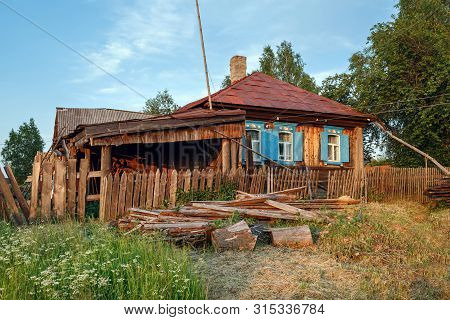 Village Street In Summer. Rickety Wooden Farmhouse With Pile Of Firewood In Front Of It. Village Of 