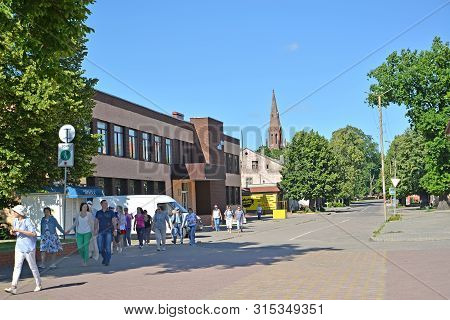 Slavsk, Russia - June 22, 2019: The Group Of Tourists Goes Along Sovetskaya Street In Summer Day. Ka