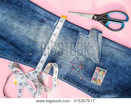 Blue Jeans With Large Hole Folded In Half, Sewing Pins In A Box, White Tailor Tape With Centimeters 
