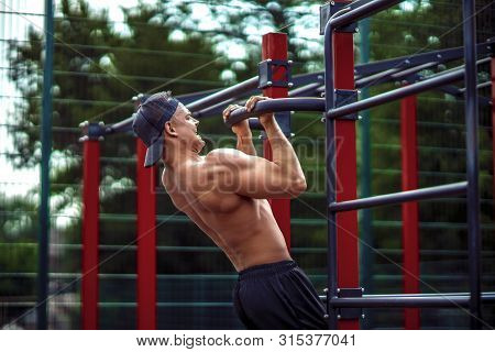 Brutal Athletic Man Making Pull-up Exercises On A Crossbar At Outdoor Streeet Gym.