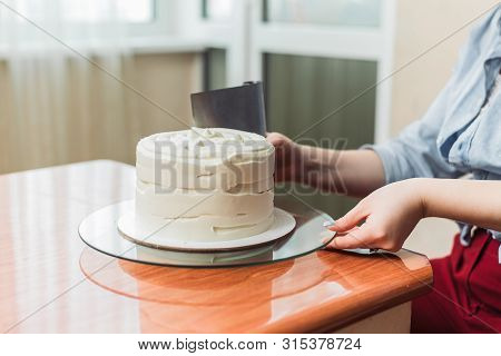 The Girl Squeezes The Cream On The Cake. A Lovely Girl Making A Cake In A Bakery. The Girl Smoothes 