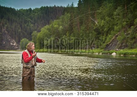 Mature Bearded Whire Wet Man Is Standing In Water In The Middle Of The River And Fishing Flyfishing,