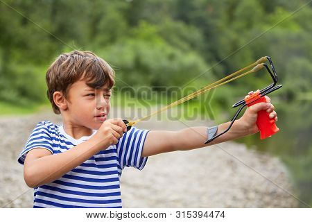White Hooligan Boy In T-shirt With Slingshot In His Hands Is Preparing For Shooting And Finding A Ta